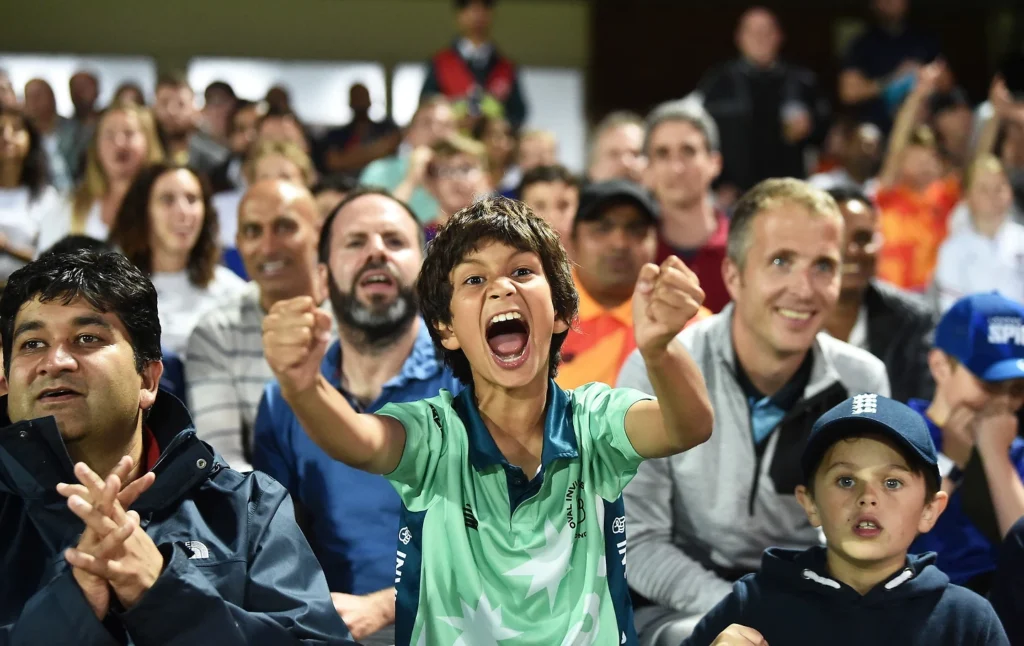Fans at a cricket match with one boy showing excitement and enthusiasm.