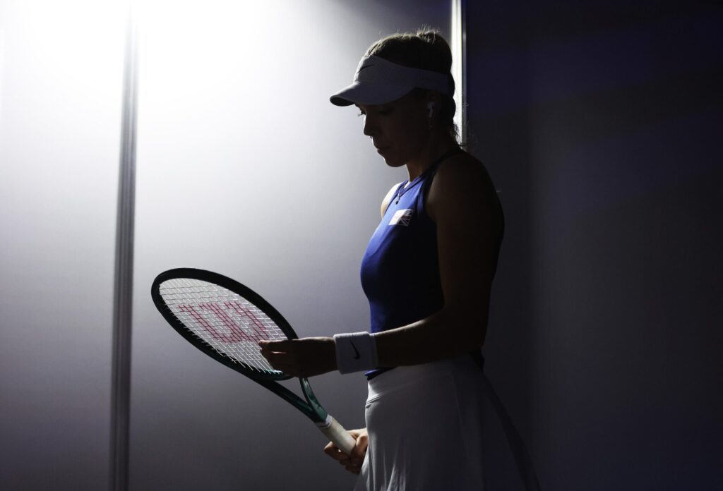 A silhouette of a female tennis player preparing to enter the court, holding a racket.