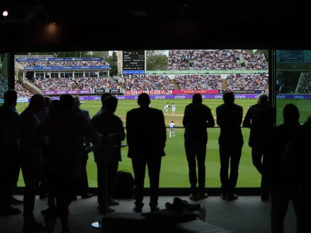 Silhouetted spectators watching a cricket match at a stadium.