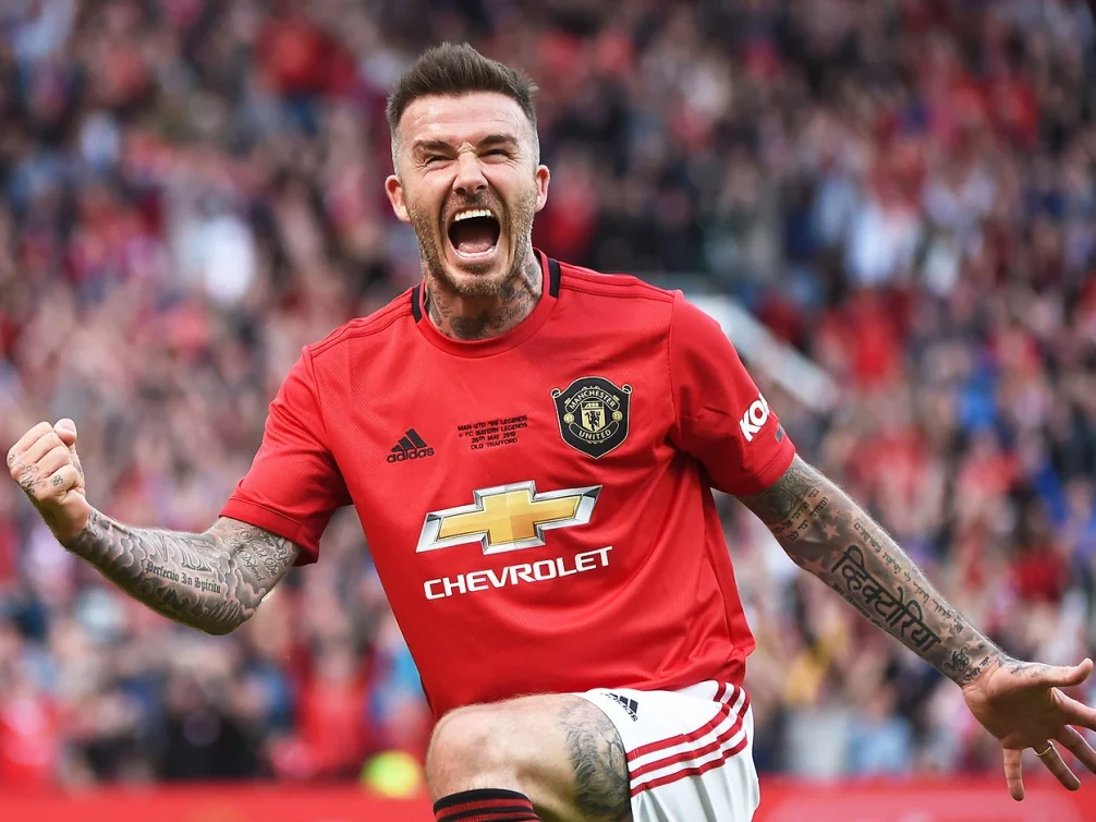 David Beckham celebrating a goal in Manchester United's red kit.