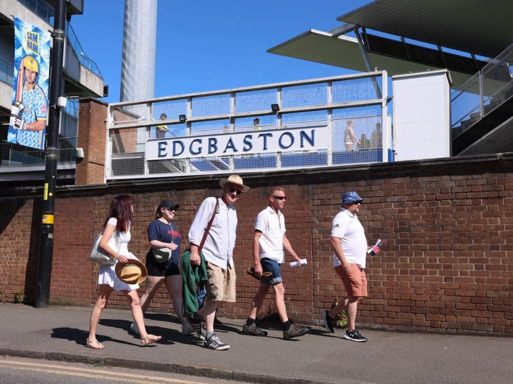 A group of cricket fans walking towards Edgbaston stadium on a sunny day.