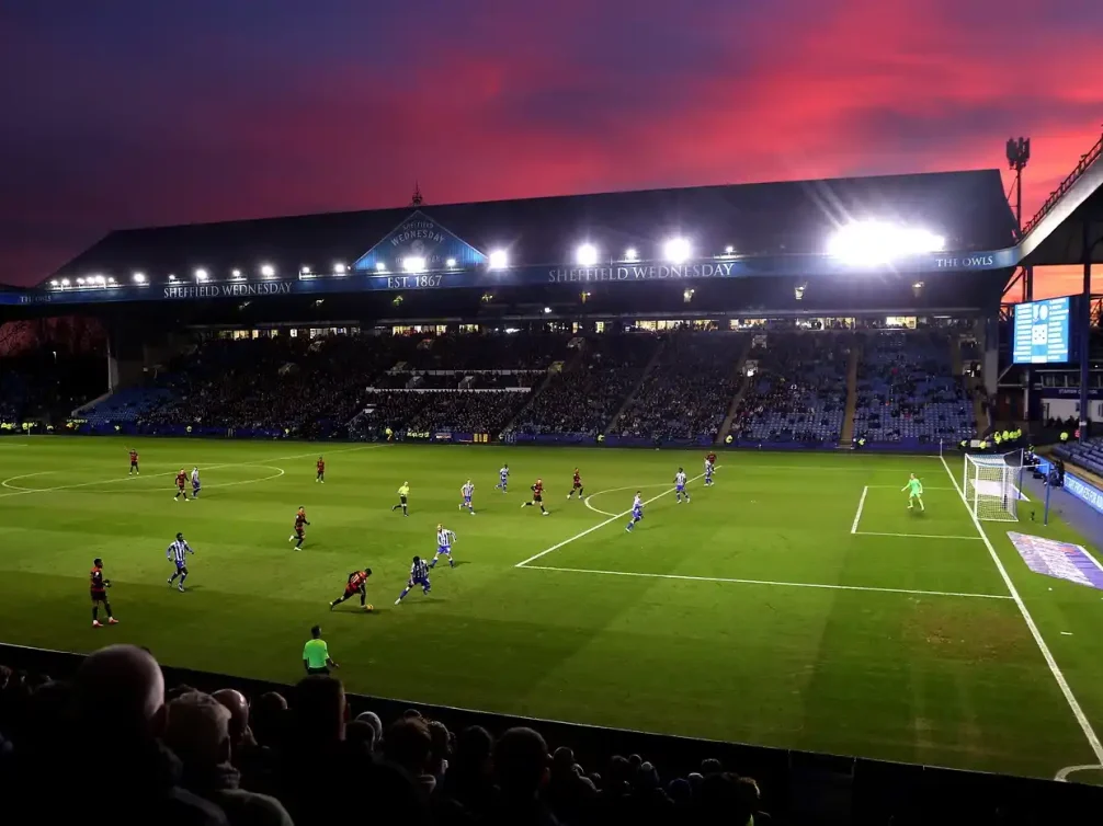 Evening football game at Sheffield Wednesday stadium with a vibrant sky.