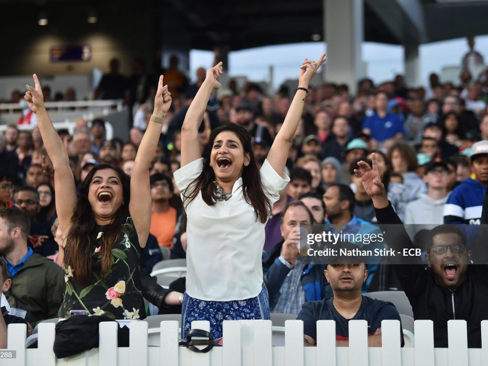 Female fans expressing excitement at a cricket stadium.