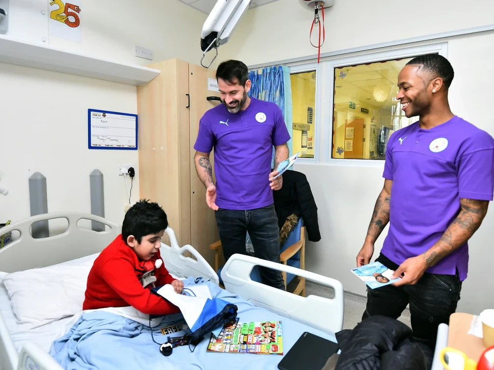A child in a hospital bed interacting with football players.