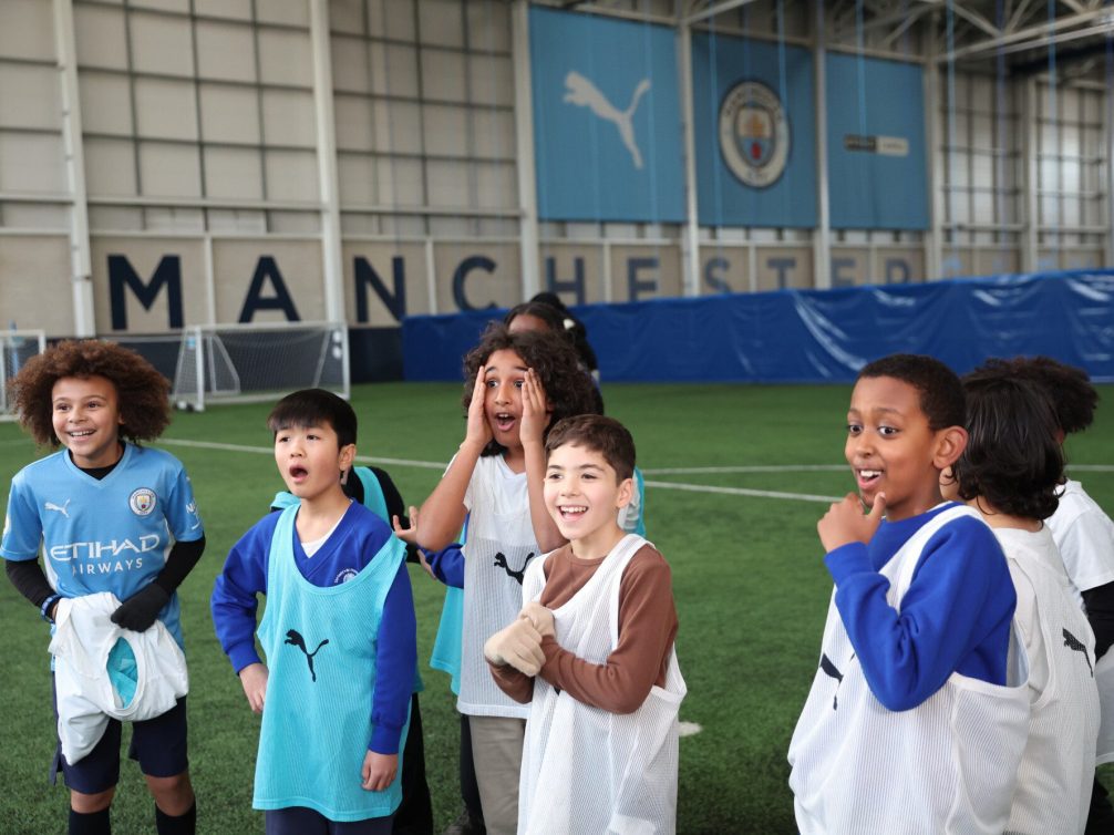 Children enjoying football training at Manchester City indoor facility.