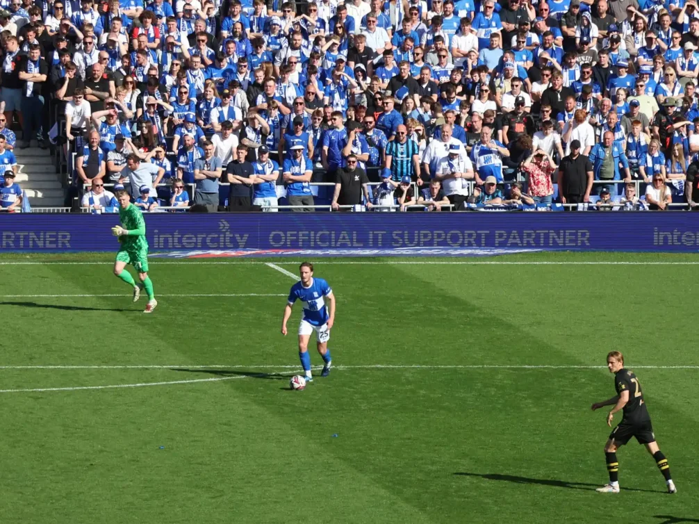 A football player in blue kit dribbling the ball during an intense match on the pitch.