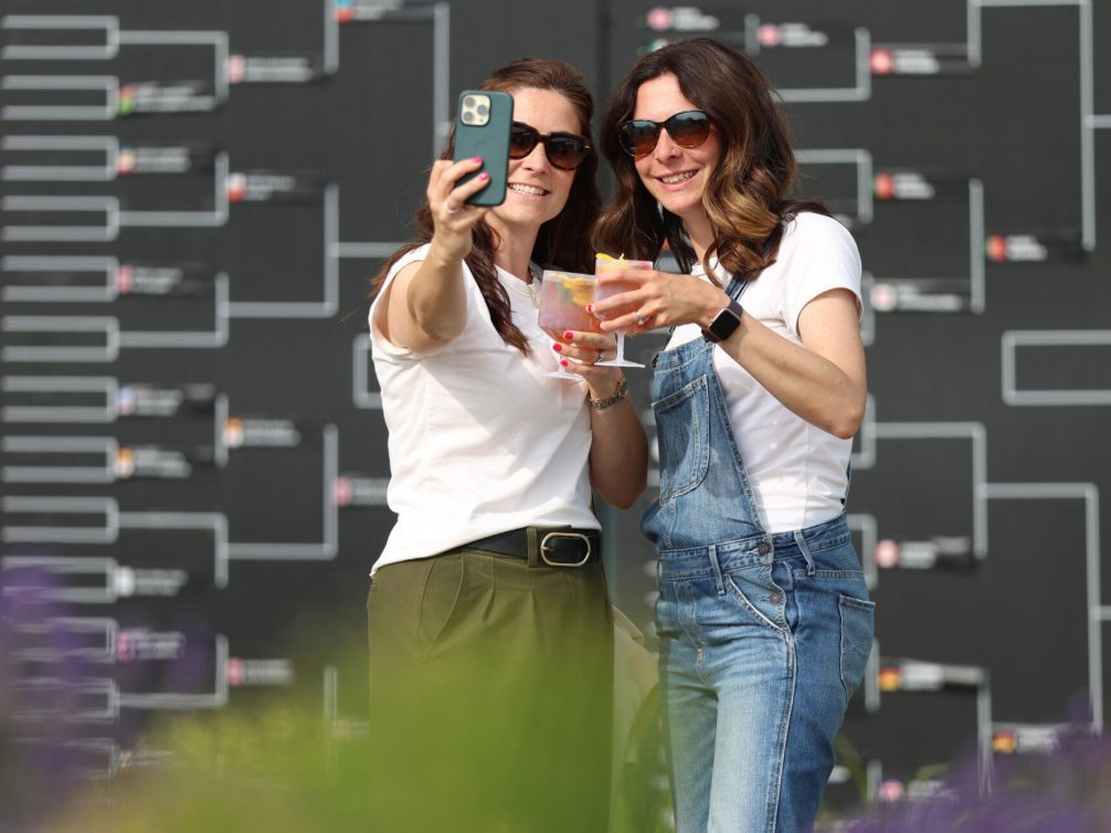 Female fans enjoying cocktails and capturing a selfie during a tennis match.