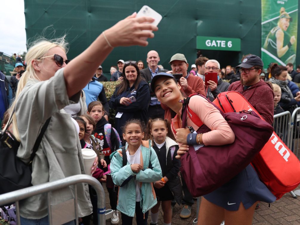 A tennis player interacting with fans, smiling and posing for photos.